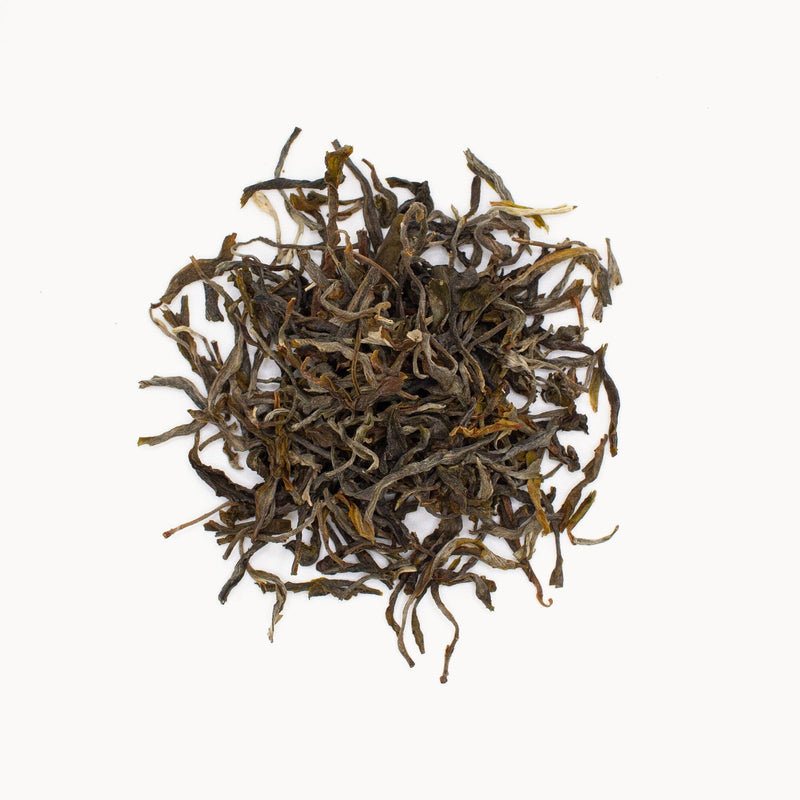 A circle of loose black tea leaves, with hints of Pu’er, is skillfully arranged on a white background, featuring Rishi Tea & Botanicals.