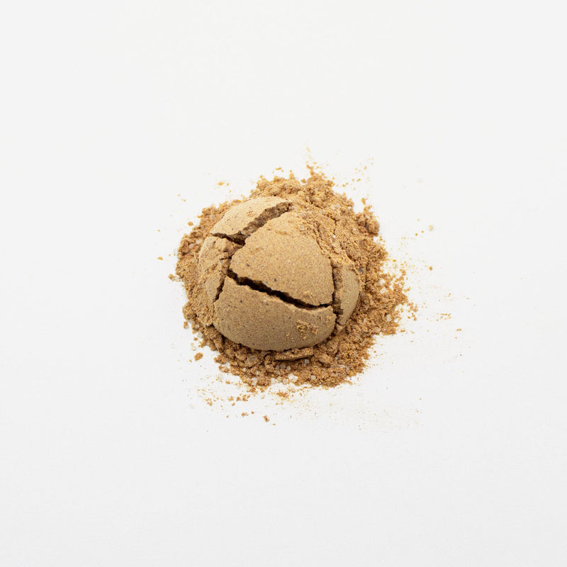 A cracked ball of Sweet Thai Tea Powder by Rishi Tea & Botanicals, with its brown, powdery appearance reminiscent of organic Thai tea, rests on a white background.