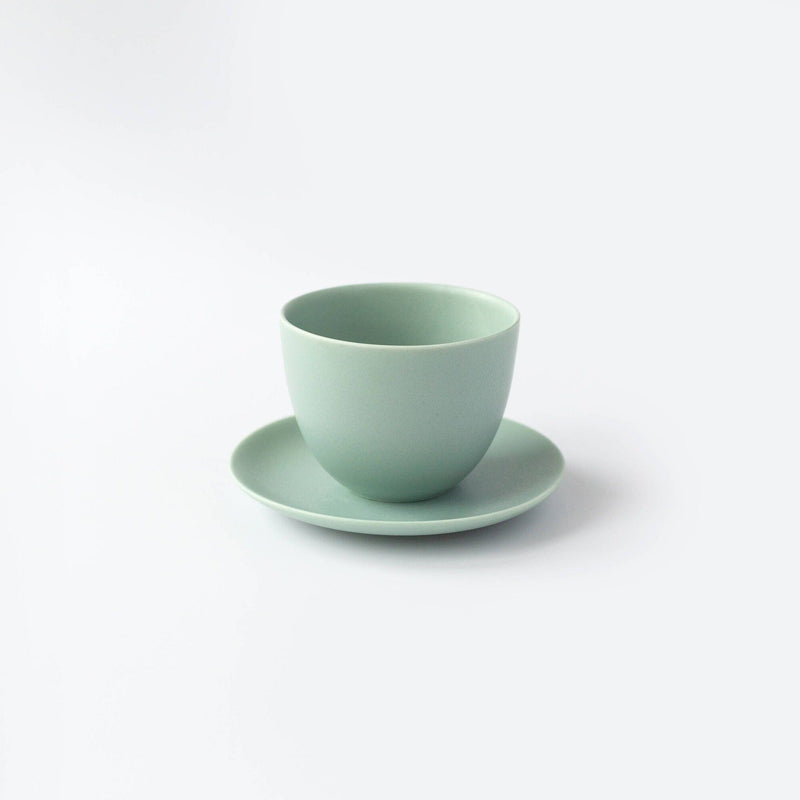 A light green pebble teacup by Kinto USA, Inc, crafted from porcelain, rests on a matching saucer against a plain white background.