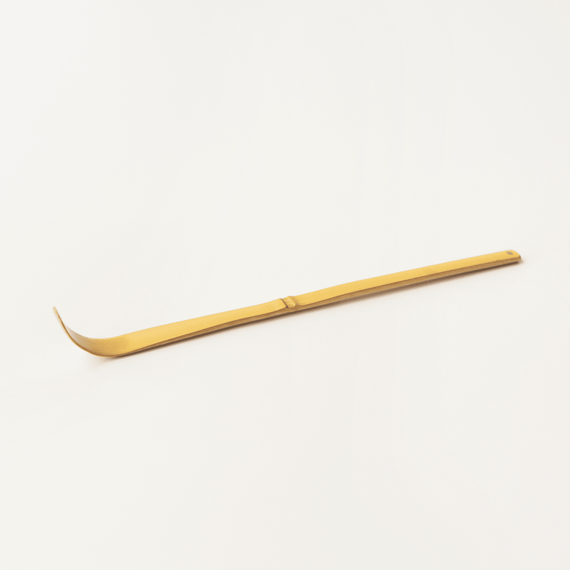 A premium bamboo matcha scoop, featuring a curved end and slender handle, elegantly complements the white background, evoking the essence of a traditional chashaku.