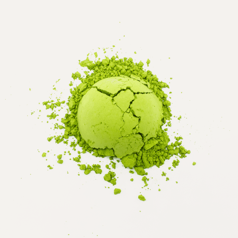 A pile of vibrant green Nishi San's Matcha Saemidori from Rishi Tea & Botanicals, infused with the rich umami flavor characteristic of this variety, partially crumbled against a pristine white background.